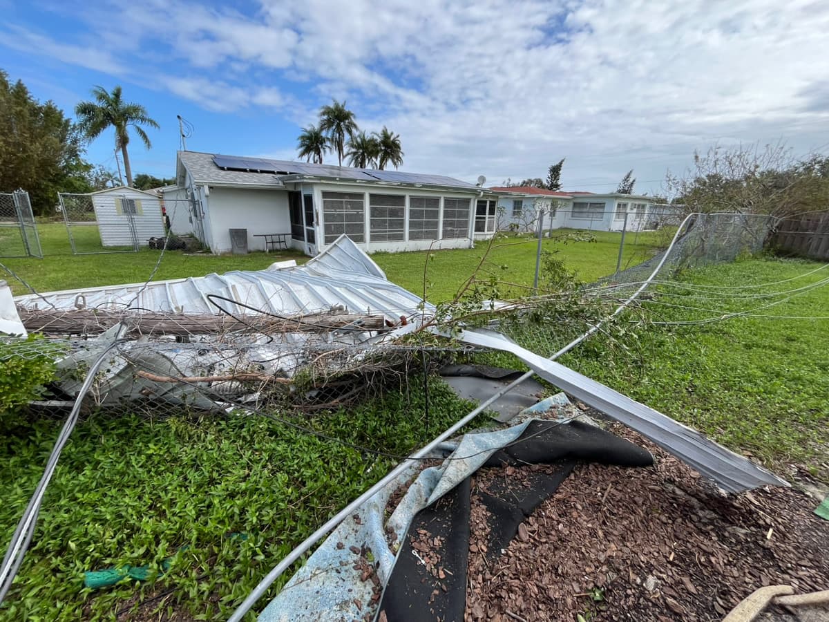 Paneles metálicos caídos y cerca dañada en una propiedad residencial